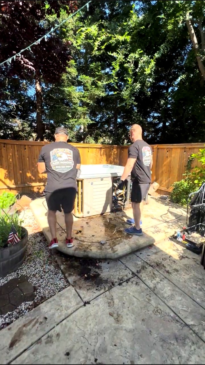 Two AMR Junk Removal crew members dismantling a backyard hot tub on a patio