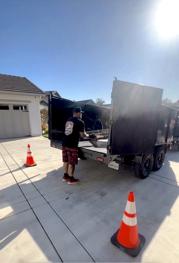 AMR Junk Removal crew member loading debris into a dump trailer on a Placer County driveway with safety cones set out